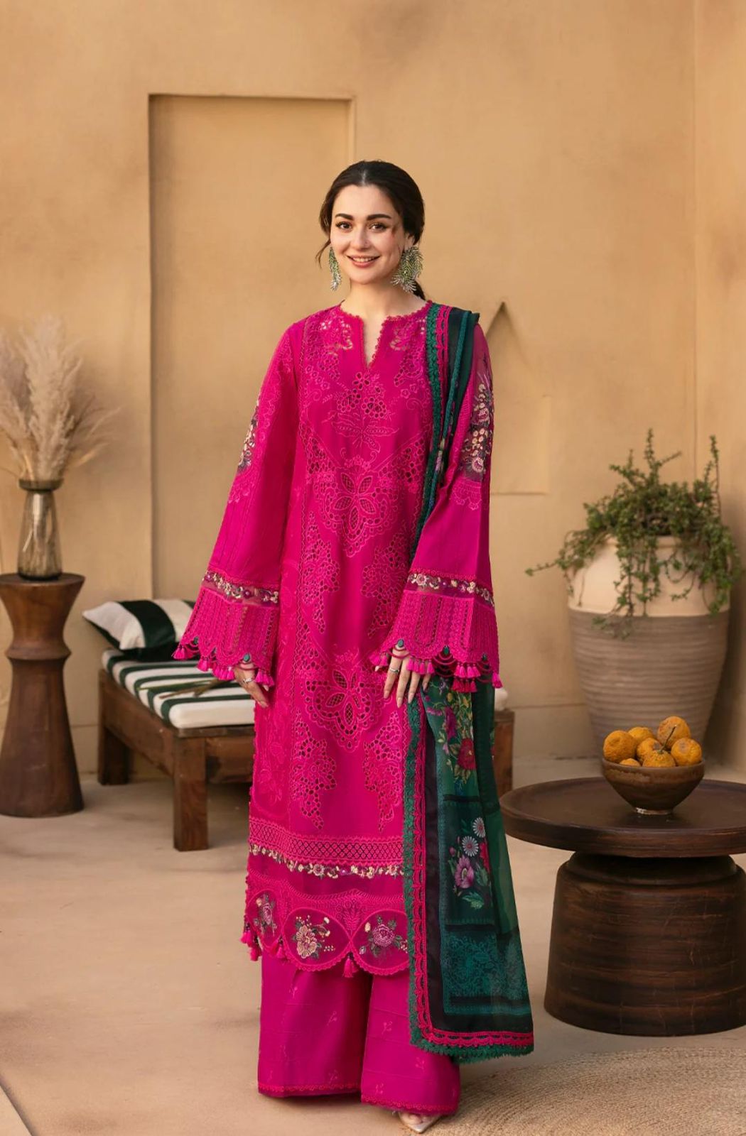 Woman in a bright pink traditional outfit with green accents standing in a room with decor elements.